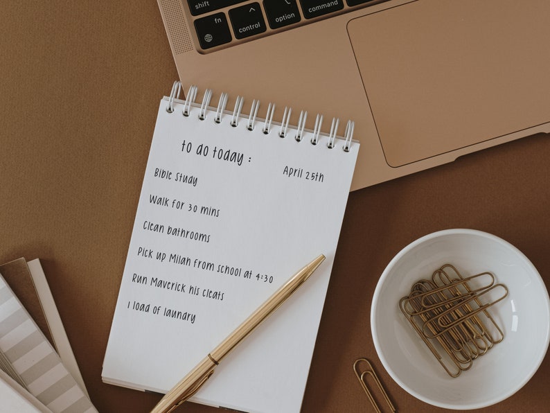 May include: A white notebook with a gold spiral binding and a to-do list for April 25th. The list includes items like "Bible Study", "Walk for 30 mins", "Clean bathrooms", "Pick up Milan from school at 4:30", "Run Maverick his cleats", and "1 load of laundry".