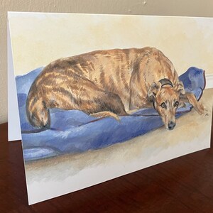 May include: A watercolor painting of a brown and black dog lying on a blue blanket. The dog has a sad expression on its face.
