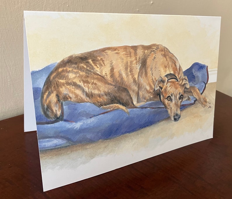 May include: A watercolor painting of a brown and black dog lying on a blue blanket. The dog has a sad expression on its face.