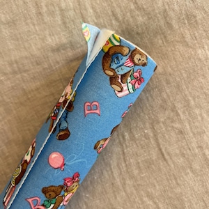 May include: Blue fabric with a white backing. The fabric has a repeating pattern of teddy bears wearing different outfits and holding gifts. The fabric also has the letter "B" printed on it.