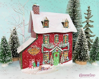 May include: A red two-storey miniature inn building with a white snow-covered roof, a green front door, and multiple windows. The sign reads The Bramley Inn. The structure is decorated with festive garlands, wreaths, and small sleds at the base.