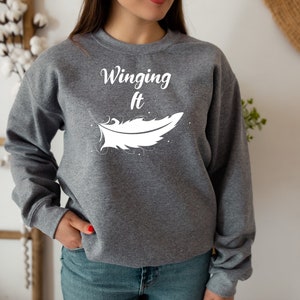 May include: Grey sweatshirt with the text "Winging It" and a white feather graphic.