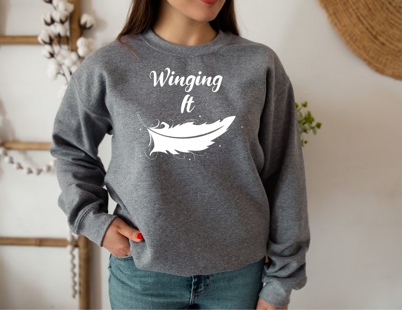 May include: Grey sweatshirt with the text "Winging It" and a white feather graphic.