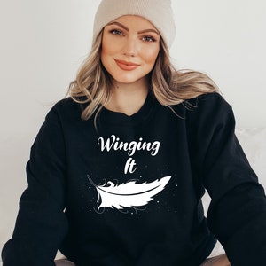May include: Black sweatshirt with white text that reads "Winging It" and a white feather graphic.