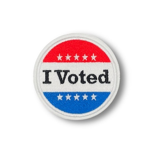 Może przedstawiać: Okrągła naklejka "Głosowałem" w kolorze białym, czerwonym i niebieskim z białymi gwiazdkami wokół krawędzi.