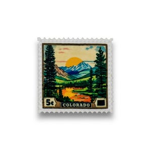 May include: A vintage 5 cent postage stamp featuring a scenic landscape of mountains, a river, and trees. The stamp is labeled "COLORADO" and has a yellow sun in the background.
