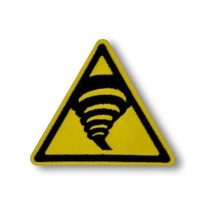 Pode incluir: Sinal de alerta triangular amarelo com contorno preto e um símbolo de tornado preto dentro.