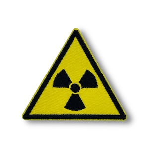 May include: Yellow triangular warning sign with a black radiation symbol inside. The sign is made of fabric and has a black border.