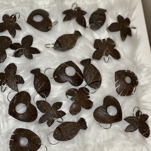 May include: A collection of 18 brown coconut shell keyrings with various shapes, including fish, hearts, butterflies, and flowers. Each keyring has a silver ring.