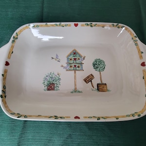 May include: Rectangular serving platter with a garden scene. The white ceramic dish features a birdhouse, trees, and birds. The rim has a decorative border with hearts and vines. Handles are on each side.