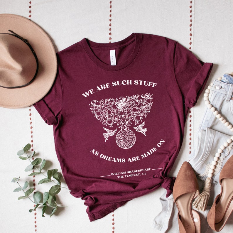 May include: A maroon t-shirt with a white graphic design featuring a tree with birds and the text "We are such stuff as dreams are made on - William Shakespeare, The Tempest, 4.1".