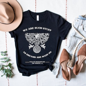 May include: Black t-shirt with a white graphic of a tree with birds and a quote from William Shakespeare's The Tempest: "We are such stuff as dreams are made on."