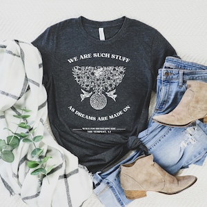 May include: A dark gray t-shirt with a white graphic design featuring a tree with birds and the quote "We are such stuff as dreams are made on." The quote is attributed to William Shakespeare, The Tempest, 4.1.