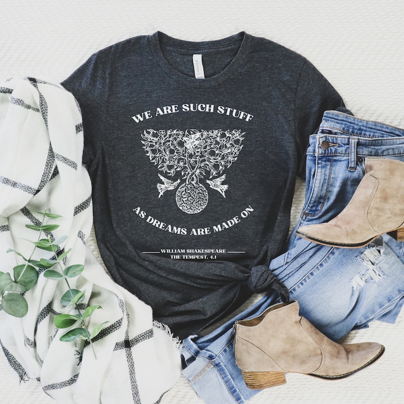 May include: A dark gray t-shirt with a white graphic design featuring a tree with birds and the quote "We are such stuff as dreams are made on." The quote is attributed to William Shakespeare, The Tempest, 4.1.