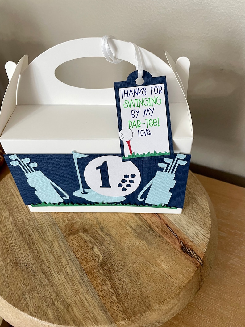 Puede incluir: Caja de regalo de fiesta de golf blanca con dise&ntilde;o azul y verde. La caja tiene un asa y una etiqueta que dice "Gracias por venir a mi par-tee! Con cari&ntilde;o."