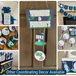 May include: Golf-themed party decorations in blue, green, and white. The decorations include a welcome sign that says "Welcome to Parker's", a banner that says "Happy Birthday", cupcake toppers, and a box with a golf bag design.