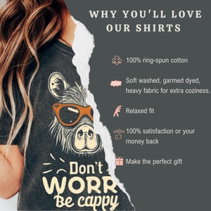 May include: A dark gray t-shirt with a cartoon llama wearing sunglasses and the text "Don't WORR Be cappy". The shirt is made of 100% ring-spun cotton and has a relaxed fit.