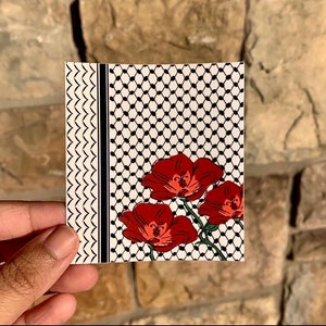 May include: A square card featuring a floral design. The card has a black and white pattern on the right side and a decorative border on the left. Three red flowers with green stems are in the center.