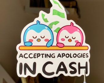 May include: A sticker featuring two cartoon penguins, one blue and one pink, with closed eyes. The sticker reads "ACCEPTING APOLOGIES IN CASH" with dollar bills above the penguins.
