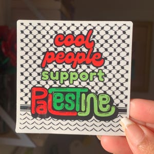 May include: A white sticker with a black and white patterned background. The sticker features the text "cool people support Palestine" in red, green, and black lettering.