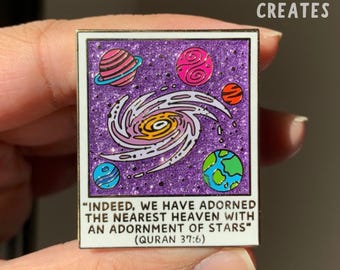 May include: A purple glitter enamel pin with a galaxy design and the quote "INDEED, WE HAVE ADORNED THE NEAREST HEAVEN WITH AN ADORNMENT OF STARS" (QURAN 37:6).