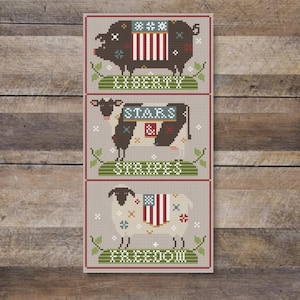 Może przedstawiać: Wzór haftu krzyżykowego przedstawiający trzy zwierzęta gospodarskie z motywami amerykańskiej flagi. Świnia jest oznaczona jako "Liberty", krowa jako "Stars & Stripes", a owca jako "Freedom".