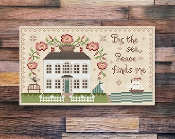 A paz me encontra, uma casa grande, uma cesta de flores, uma menina à beira-mar, padrão de ponto cruz de arte folclórica primitiva da Acadia Stitchery.
