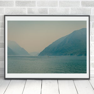 Könnte beinhalten: Ein gerahmtes Foto einer nebeligen, blaugrünen Bergkette, die sich in einem stillen Gewässer spiegelt. Die Berge sind in der Ferne, das Wasser im Vordergrund. Es befinden sich ein paar kleine Boote im Wasser.