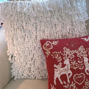 May include: A white fluffy throw pillow with a red beaded pillow with a white reindeer design on it.