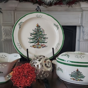 Könnte beinhalten: Ein Set aus drei weißen Keramik-Weihnachtsbaum-Tellern mit grünem Rand. Die Teller zeigen einen grünen Weihnachtsbaum mit Ornamenten und einem roten Band. Das Set beinhaltet eine große Platte, eine kleine Schüssel und eine geschlossene Auflaufform.