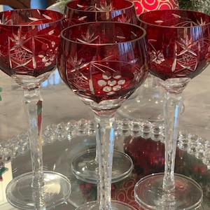 May include: Set of four red wine glasses with intricate cut glass designs. The glasses have a clear stem and base.