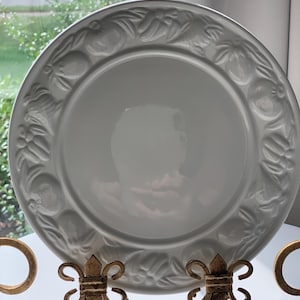 Puede incluir: Plato de cena de cerámica blanca con un diseño en relieve de frutas y hojas alrededor del borde.