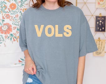 May include: A light blue t-shirt with the word "VOLS" in large, orange and white checkered letters.