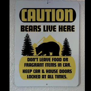 May include: A white metal sign with black and yellow text that reads "CAUTION BEARS LIVE HERE DON'T LEAVE FOOD OR FRAGRANT ITEMS IN CAR. KEEP CAR & HOUSE DOORS LOCKED AT ALL TIMES."