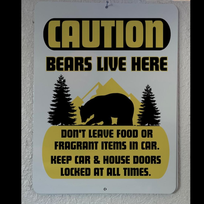 May include: A white metal sign with black and yellow text that reads "CAUTION BEARS LIVE HERE DON'T LEAVE FOOD OR FRAGRANT ITEMS IN CAR. KEEP CAR & HOUSE DOORS LOCKED AT ALL TIMES."
