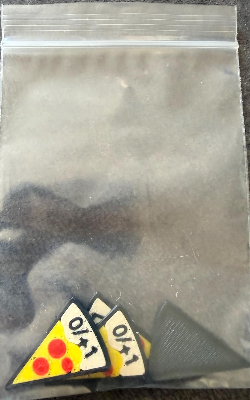May include: A clear plastic resealable bag containing several triangular game tokens. The tokens feature a yellow and white pizza slice design with red pepperoni circles and the black text 0/+1 printed on the surface, alongside solid grey tokens.