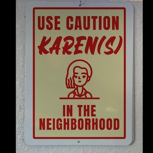 May include: A red and white sign with the text "Use Caution Karen(s) in the Neighborhood". A cartoon image of a woman with short hair is in the center of the sign.