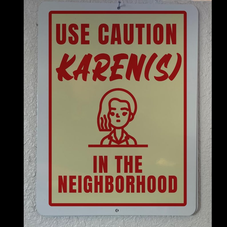 May include: A red and white sign with the text "Use Caution Karen(s) in the Neighborhood". A cartoon image of a woman with short hair is in the center of the sign.