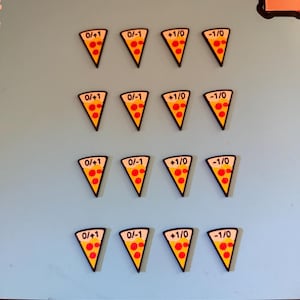 May include: Sixteen triangular pizza slice tokens arranged in four rows of four. Each token features a yellow crust, red pepperoni circles, and black text reading 0/+1, 0/-1, +1/0, or -1/0. The tokens have a black border and are set on a light blue surface.