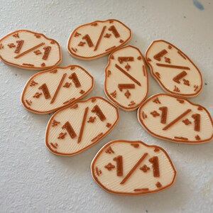 K&ouml;nnte beinhalten: Sieben cremefarbene, unregelm&auml;&szlig;ig geformte Spielsteine mit erhabenen, kupferfarbenen Details. Jeder Spielstein zeigt mittig den Text 1/1, flankiert von kleinen vierzackigen Sternsymbolen. Die Oberfl&auml;che weist eine feine, 3D-gedruckte Linienstruktur auf.