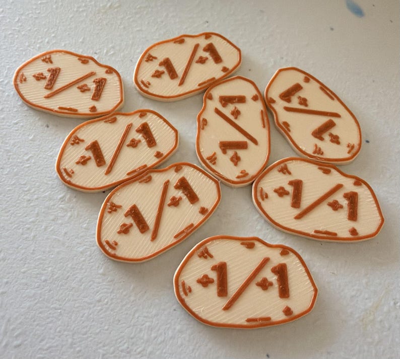 K&ouml;nnte beinhalten: Sieben cremefarbene, unregelm&auml;&szlig;ig geformte Spielsteine mit erhabenen, kupferfarbenen Details. Jeder Spielstein zeigt mittig den Text 1/1, flankiert von kleinen vierzackigen Sternsymbolen. Die Oberfl&auml;che weist eine feine, 3D-gedruckte Linienstruktur auf.