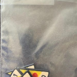 May include: A collection of small, triangular pizza slice charms inside a clear plastic resealable bag. Each charm features a yellow crust, white cheese, and red pepperoni dots, with the fraction 1/0 printed in black ink on the white surface.