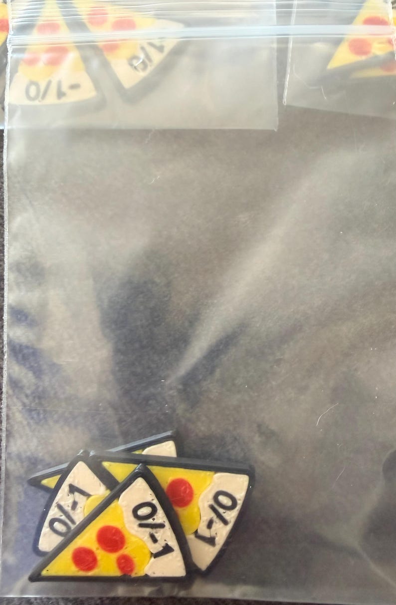May include: A collection of small, triangular pizza slice charms inside a clear plastic resealable bag. Each charm features a yellow crust, white cheese, and red pepperoni dots, with the fraction 1/0 printed in black ink on the white surface.