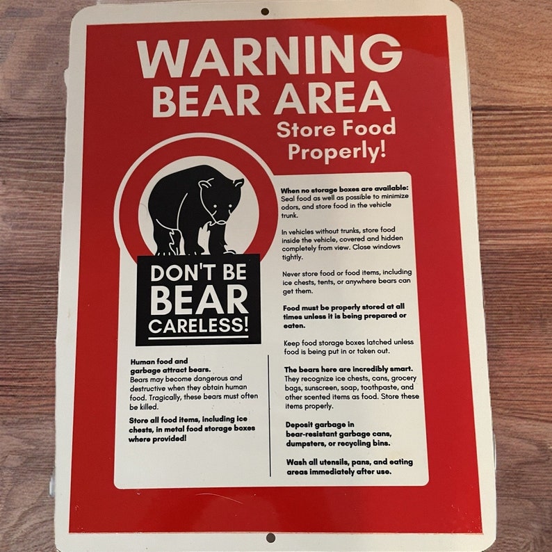 May include: A red and white warning sign with a black bear illustration. The sign reads "Warning Bear Area Store Food Properly!" and includes instructions on how to store food properly to avoid attracting bears. The sign also includes the text "Don't Be Bear Careless!"