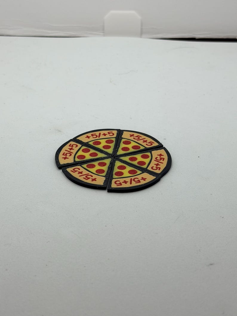 May include: A circular game token shaped like a pizza, divided into six individual triangular slices. Each slice features a yellow crust, red pepperoni dots, and the text +5/+5 printed in red. The entire token has a black border.