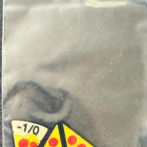 May include: Three triangular pizza slice charms inside a clear plastic resealable bag. Each charm features a yellow cheese surface with red pepperoni circles and a white crust edge printed with the black text -1/0 in a bold sans-serif font.