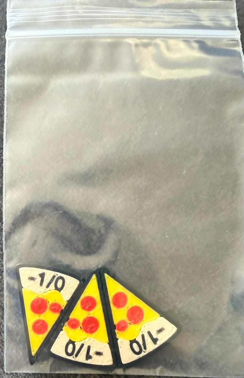 May include: Three triangular pizza slice charms inside a clear plastic resealable bag. Each charm features a yellow cheese surface with red pepperoni circles and a white crust edge printed with the black text -1/0 in a bold sans-serif font.