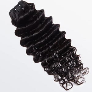 May include: A bundle of wavy, black human hair extensions. The hair is thick, with a deep wave pattern, and appears to be of high quality. The extensions are neatly bundled at the top, ready for application. The hair is a rich, dark black color.