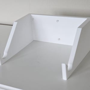 May include: White wall-mounted shelf with two hooks, designed to hold a guitar or other items.