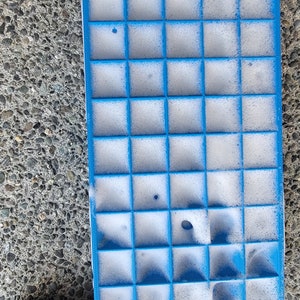 May include: A blue plastic ice cube tray filled with white foam. The tray has 36 individual compartments.